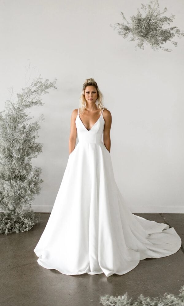 Phillips by Tara LaTour Bridal at Love and Lace Bridal Salon in Orange, CA: matte satin A-line wedding gown with deep V-neck and pockets with a long train.