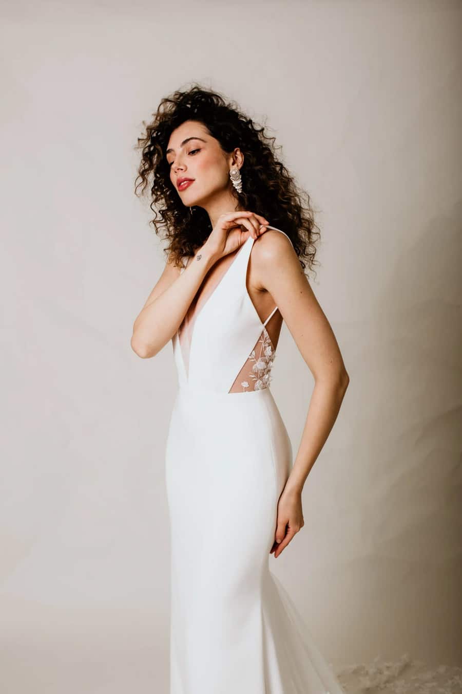 Hutton by Anais Anette Bridal is a blend of modern romance, sleek design, and delicate detailing, featuring a fitted crepe silhouette with a deep V-neckline, an open back, and delicate 3D floral details, beading, embroidery, and sequins on the side panels available at Love and Lace Bridal Salon in Orange County, CA.