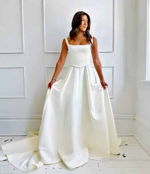 Tara LaTour Sherlock: A stunning basque waist wedding dress in matte satin with a modern square neckline and elegant cathedral train at Love and Lace Bridal Salon in Orange, CA