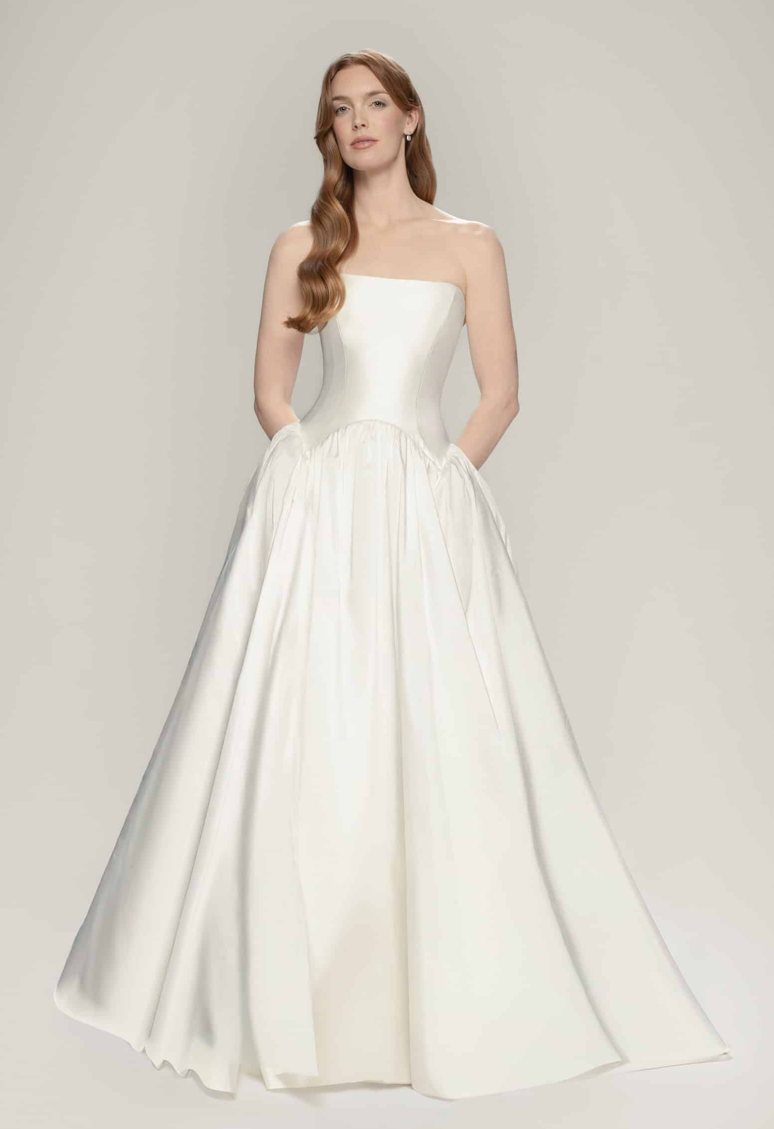 Ines wedding dress by Aesling Bridal available at Love and Lace Bridal Salon in Orange, CA, featuring a classic taffeta strapless scoop neckline, an architectural double-pointed reverse basque dropped waist, and a voluminous full circle skirt with an 80-inch train.