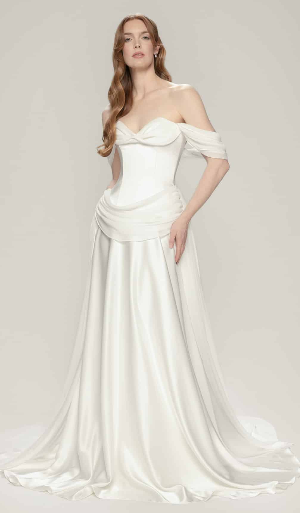 Paloma wedding dress by Aesling Bridal available at Love and Lace Bridal Salon in Orange, CA. A luminous satin gown featuring a strapless sweetheart neckline, reverse basque dropped waist, and a half-circle skirt with a 60-inch train, shown with its signature detachable chiffon bust cowl and off-shoulder swag sleeves.